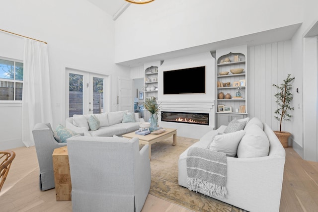 living room featuring built in features, light hardwood / wood-style flooring, and high vaulted ceiling