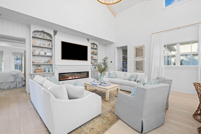 living room with built in features, light hardwood / wood-style floors, and a high ceiling