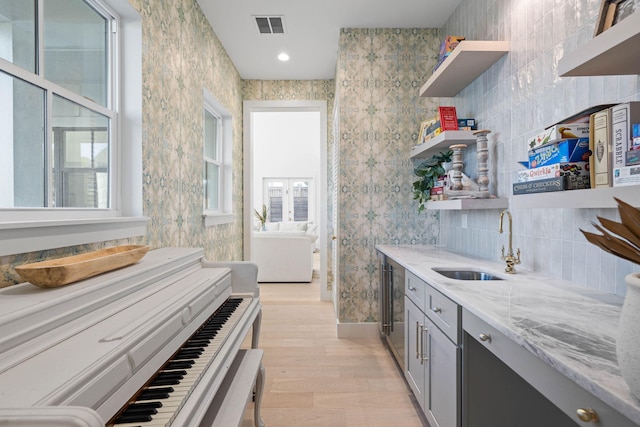 kitchen with gray cabinetry, light stone counters, light wood-type flooring, and sink