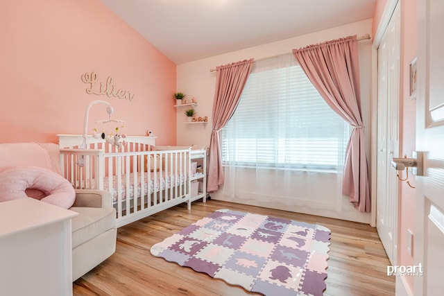 bedroom featuring light wood-type flooring, lofted ceiling, and a nursery area