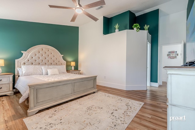 bedroom with ceiling fan, light hardwood / wood-style floors, and a towering ceiling