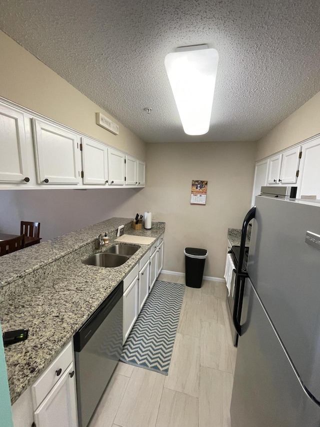 kitchen featuring white cabinets, sink, a textured ceiling, appliances with stainless steel finishes, and light stone counters