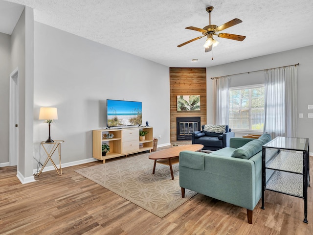 living room with a textured ceiling, ceiling fan, wood-type flooring, and a fireplace