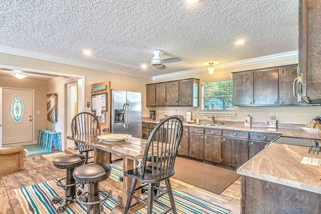 kitchen featuring stainless steel fridge, dark brown cabinets, ceiling fan, crown molding, and sink