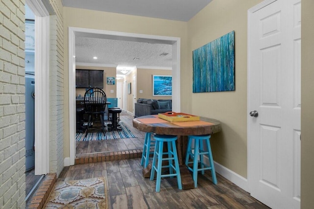 dining space with dark hardwood / wood-style flooring, a textured ceiling, and ornamental molding