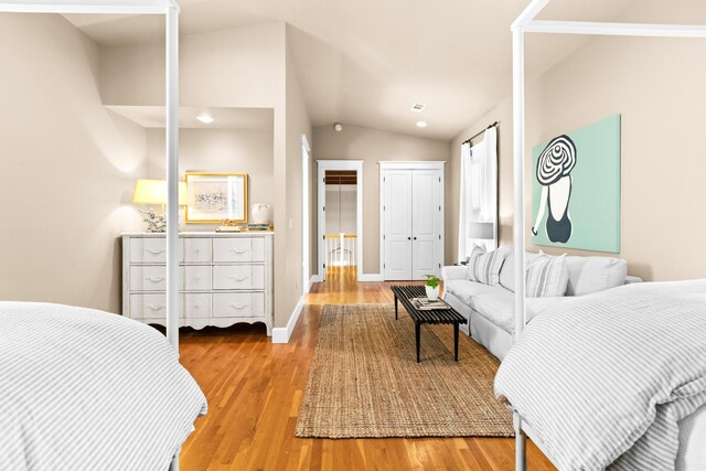 bedroom featuring a closet, vaulted ceiling, light wood-style flooring, and baseboards