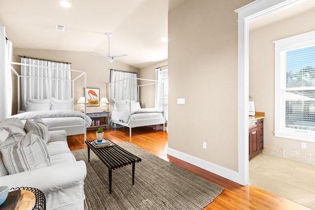 bedroom featuring visible vents, light wood-style flooring, vaulted ceiling, ensuite bath, and baseboards