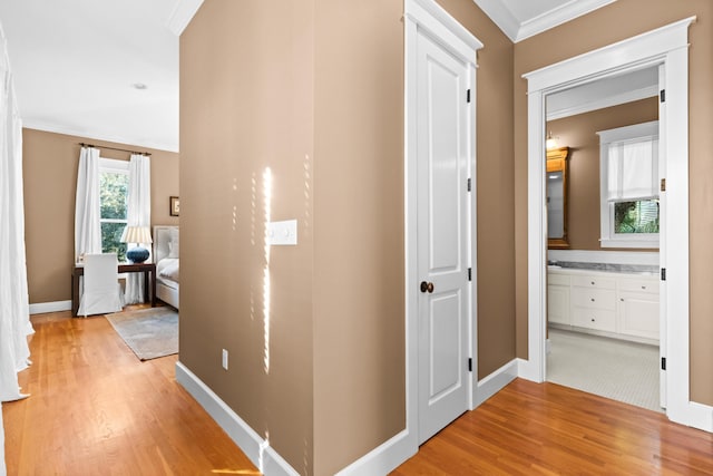 hallway featuring light wood-type flooring, crown molding, and baseboards