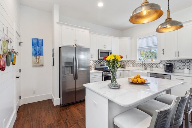 kitchen featuring light stone counters, a center island, decorative light fixtures, stainless steel appliances, and white cabinets