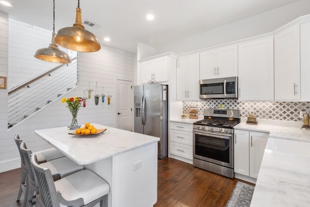 kitchen with light stone counters, appliances with stainless steel finishes, white cabinetry, and hanging light fixtures