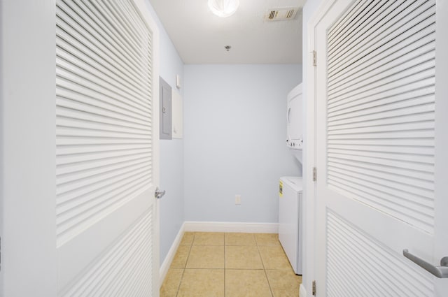 clothes washing area featuring electric panel, stacked washer and dryer, and light tile patterned floors