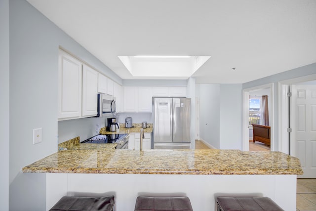 kitchen featuring white cabinetry, stainless steel appliances, kitchen peninsula, a breakfast bar area, and light tile patterned flooring