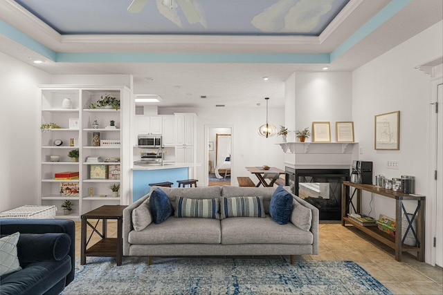 tiled living room with a raised ceiling, ceiling fan, sink, and a multi sided fireplace