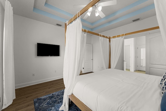 bedroom with ceiling fan, dark wood-type flooring, and a tray ceiling