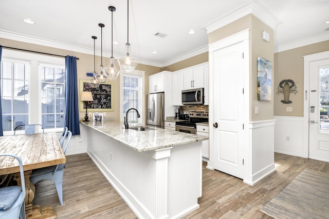 kitchen featuring light stone countertops, appliances with stainless steel finishes, crown molding, pendant lighting, and light hardwood / wood-style flooring