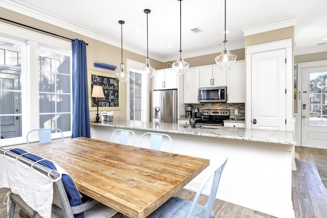 kitchen featuring white cabinetry, hanging light fixtures, light stone counters, light hardwood / wood-style floors, and appliances with stainless steel finishes