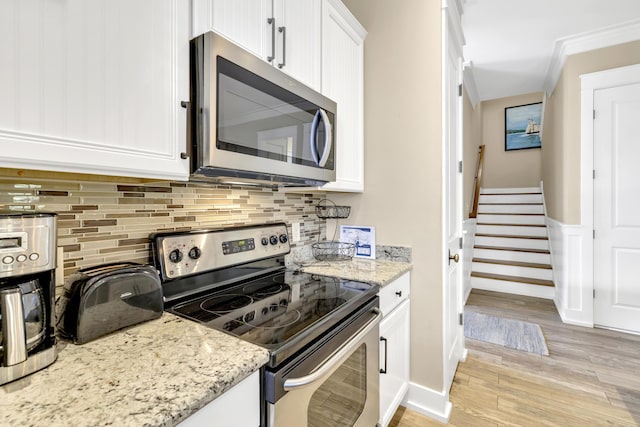 kitchen with white cabinets, light stone countertops, ornamental molding, light hardwood / wood-style floors, and stainless steel appliances