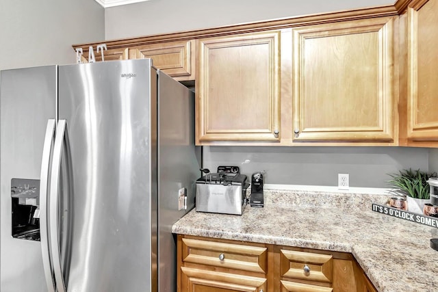 kitchen with light stone counters, light brown cabinets, and stainless steel refrigerator with ice dispenser