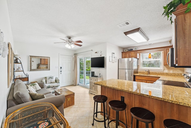 kitchen with a breakfast bar, light stone countertops, plenty of natural light, kitchen peninsula, and stainless steel appliances