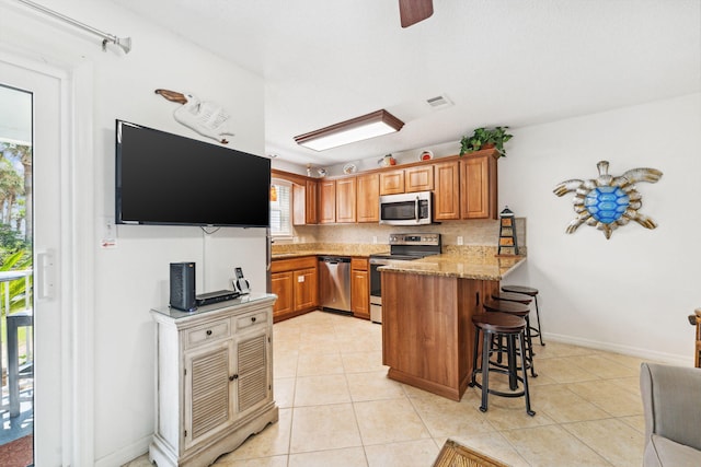 kitchen with a kitchen breakfast bar, light stone countertops, appliances with stainless steel finishes, light tile patterned flooring, and kitchen peninsula