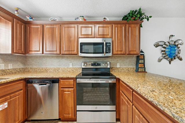 kitchen featuring appliances with stainless steel finishes, a textured ceiling, tasteful backsplash, and light stone counters