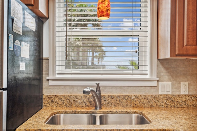 details featuring black fridge, light stone countertops, and sink