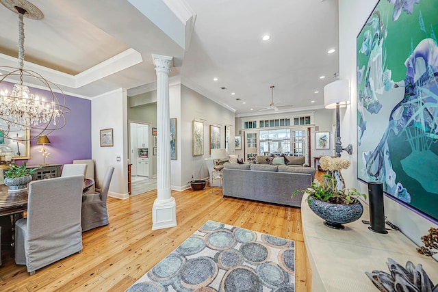 living room featuring decorative columns, crown molding, light hardwood / wood-style floors, and ceiling fan with notable chandelier