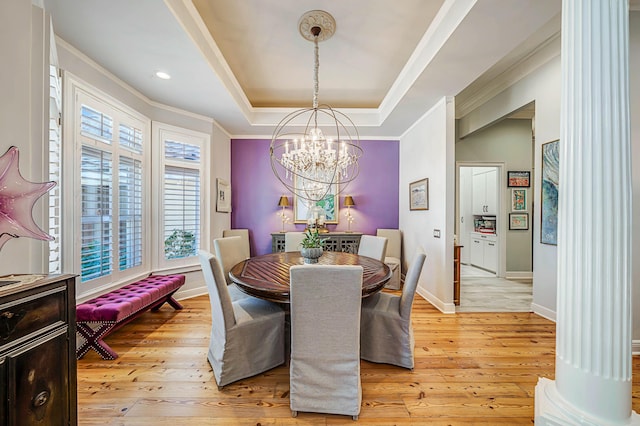 dining area featuring a raised ceiling, light wood-type flooring, ornamental molding, ornate columns, and a chandelier