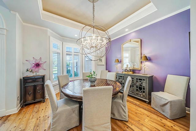 dining space featuring an inviting chandelier, light hardwood / wood-style flooring, a raised ceiling, and ornamental molding