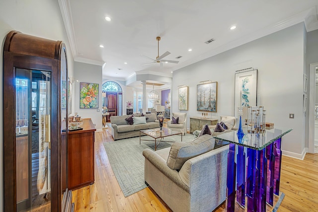 living room featuring ceiling fan with notable chandelier, light hardwood / wood-style floors, ornate columns, and ornamental molding