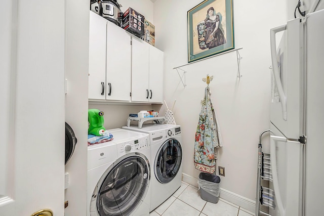 clothes washing area featuring cabinets, light tile patterned floors, and washer and clothes dryer