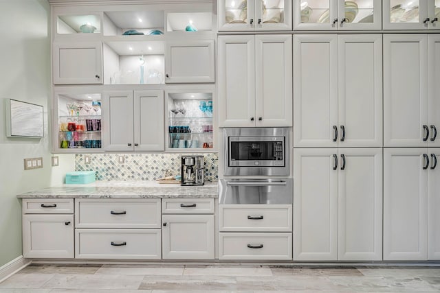 bar featuring white cabinetry, tasteful backsplash, light stone counters, and stainless steel microwave