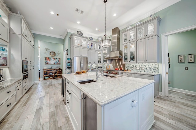 kitchen featuring exhaust hood, a center island with sink, hanging light fixtures, sink, and stainless steel appliances