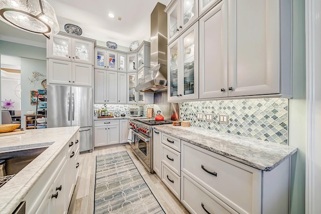 kitchen featuring light stone countertops, wall chimney exhaust hood, backsplash, decorative light fixtures, and appliances with stainless steel finishes