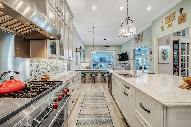 kitchen with exhaust hood, white cabinets, a center island with sink, hanging light fixtures, and stainless steel appliances