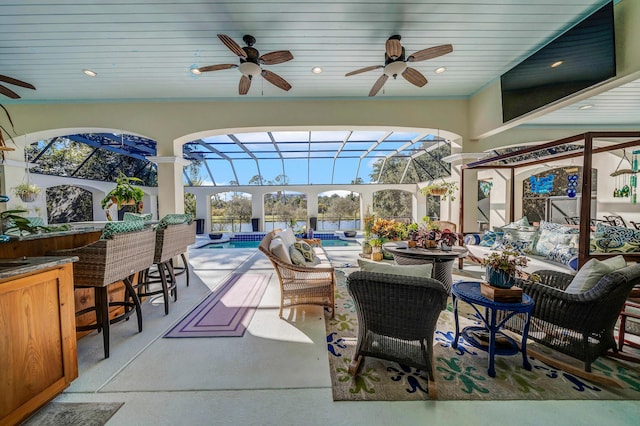 view of patio featuring ceiling fan, an outdoor hangout area, exterior bar, and glass enclosure