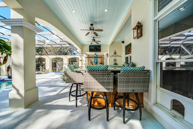 view of patio featuring a lanai, ceiling fan, and a bar