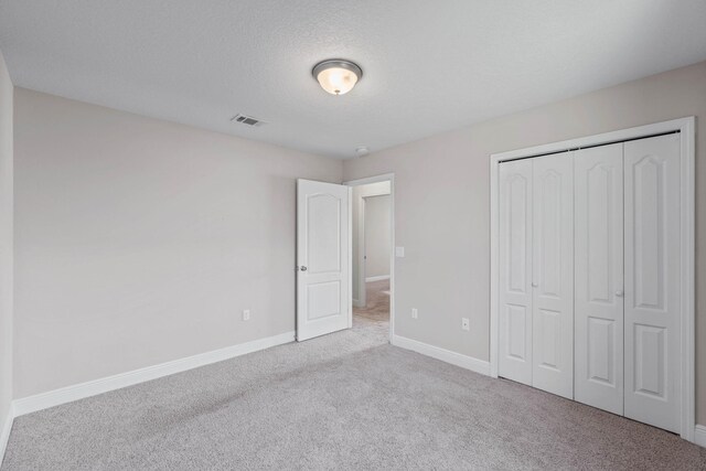 unfurnished bedroom with light carpet, a textured ceiling, and a closet