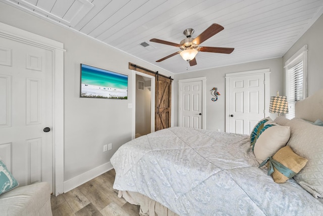 bedroom featuring ceiling fan, a barn door, light wood-type flooring, and wooden ceiling