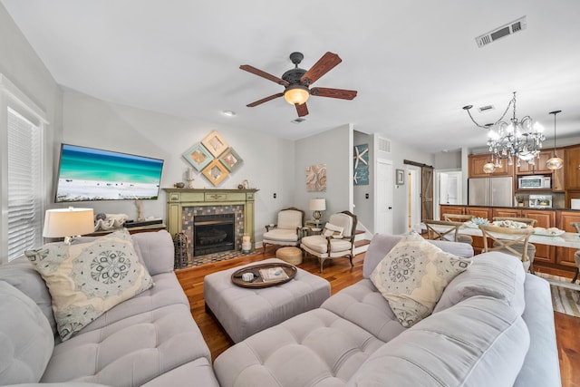 living room featuring a fireplace, wood-type flooring, and ceiling fan with notable chandelier