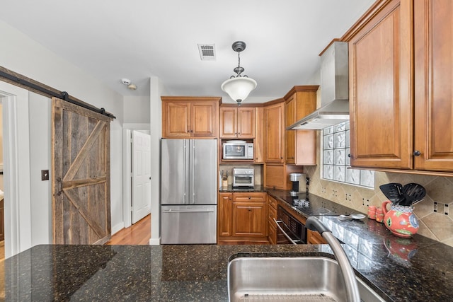 kitchen with wall chimney range hood, a barn door, black oven, decorative light fixtures, and high end fridge