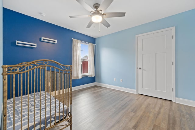 unfurnished bedroom with ceiling fan, a nursery area, and hardwood / wood-style flooring