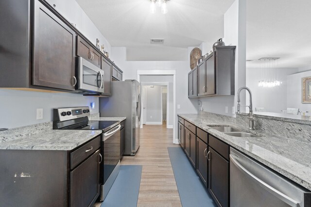 kitchen featuring sink, light stone countertops, dark brown cabinets, light hardwood / wood-style floors, and stainless steel appliances