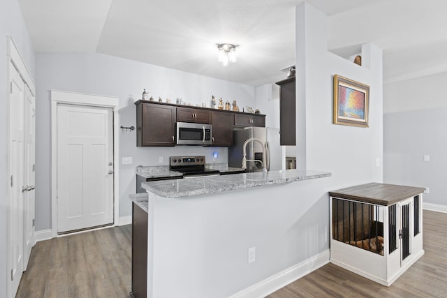 kitchen with kitchen peninsula, light stone counters, dark brown cabinetry, stainless steel appliances, and wood-type flooring