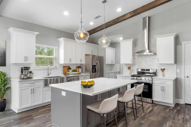 kitchen with wall chimney range hood, hanging light fixtures, stainless steel appliances, white cabinets, and a kitchen island