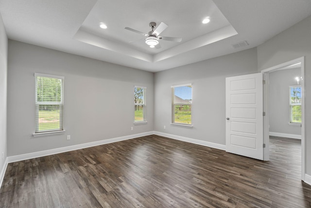 empty room with dark hardwood / wood-style floors, a raised ceiling, and ceiling fan