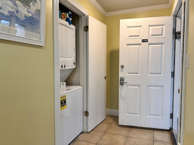 washroom with a textured ceiling, light tile patterned flooring, ornamental molding, and stacked washer and dryer