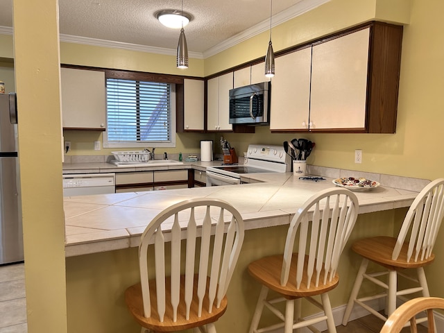 kitchen with kitchen peninsula, a textured ceiling, white appliances, hanging light fixtures, and a breakfast bar area