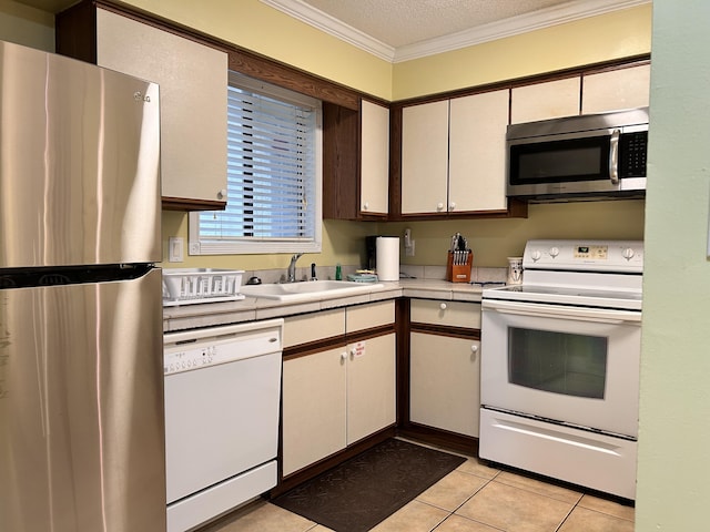 kitchen with sink, stainless steel appliances, a textured ceiling, light tile patterned flooring, and ornamental molding