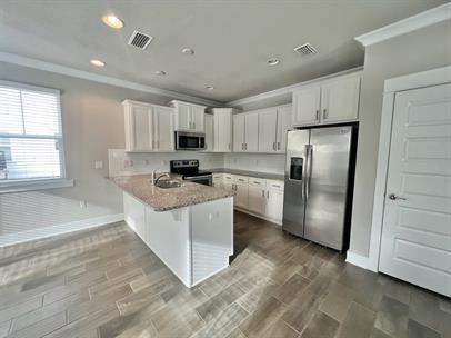 kitchen with stainless steel appliances, light stone counters, kitchen peninsula, a breakfast bar, and white cabinets